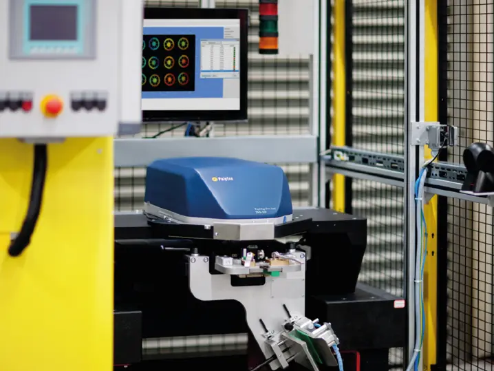 Polytec ToughMetrology laser sensor scanning an industrial component with data displayed on a nearby monitor in a lab setting.