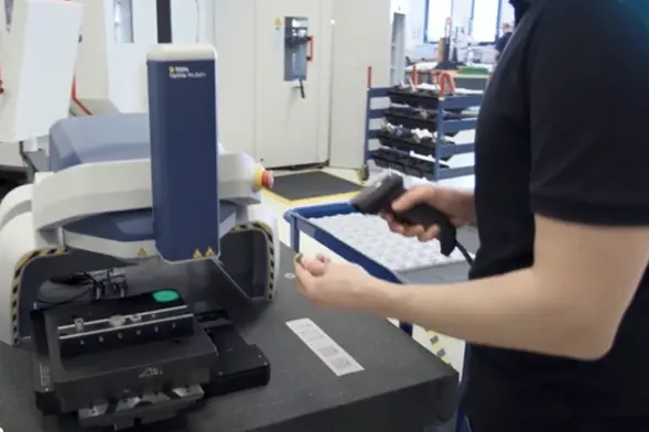 Operator using a handheld barcode scanner to inspect components on a Polytec precision measurement device in a manufacturing lab.