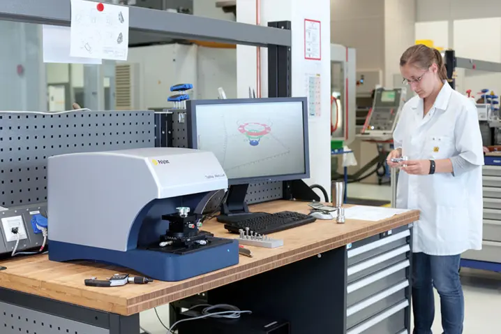 Technician in a lab coat operating Polytec optical 3D surface profiler with 3D measurement software on a desktop monitor.