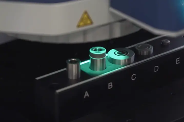 Close-up of a microscope-based 3D surface profiler analyzing precision-engineered metal components with green illumination.