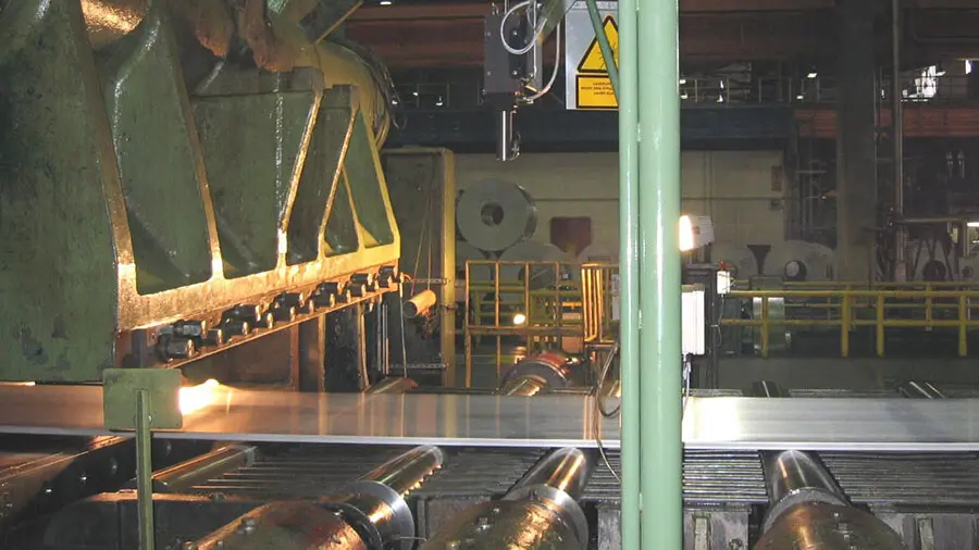 Industrial metal sheet production line showing laser speed sensor monitoring continuous steel sheet movement for process control.