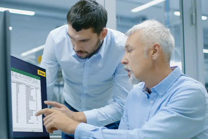 Two engineers analyzing data on a computer screen in a modern industrial facility, discussing measurements.