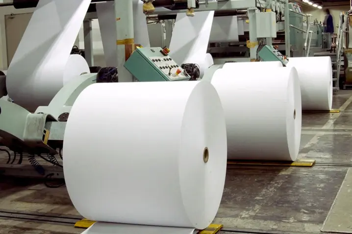 Large white paper rolls feeding into an industrial machine for continuous length measurement and processing.