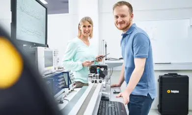 Two engineers collaborating on precision optical measurement equipment with Polytec branding in a bright lab setting.