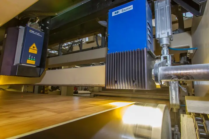 Blue Baumer optical sensor measuring length and speed of wooden sheet on conveyor belt in an industrial production line